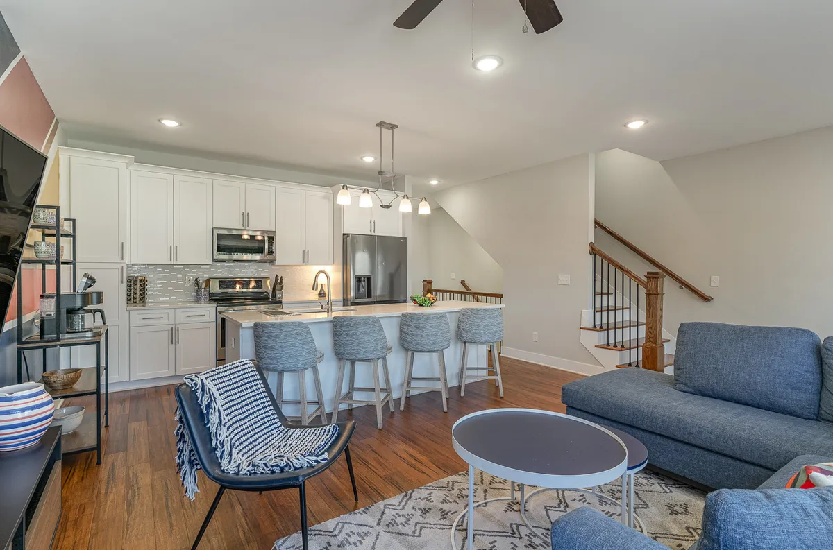 This interior image presents an open kitchen and living room, featuring a kitchen island, sofa, and staircase. The space exudes comfort and versatility, ideal for family game nights, cooking together, or simply unwinding after a day of adventure.