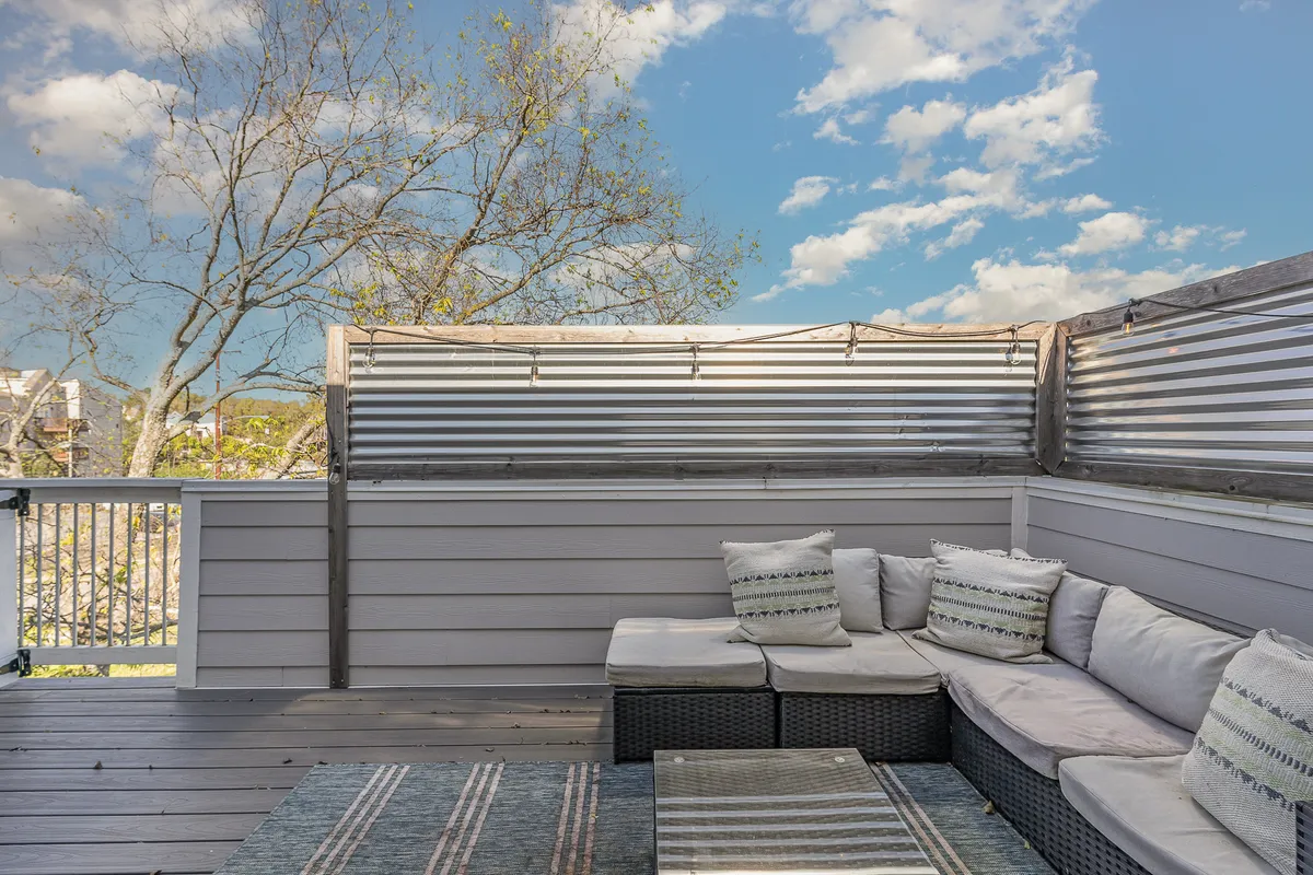 An inviting outdoor seating area adorned with decorative cushions and a textured rug, set against a backdrop of greenery. The space is perfect for socializing, relaxing with friends, or celebrating together, especially as the sun sets.