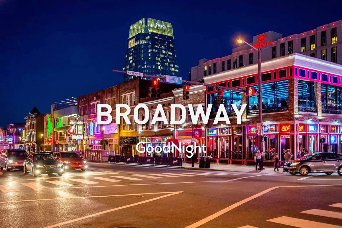 A lively nighttime street scene along a bustling stretch of Nashville. Neon signs shine overhead while crowds of people walk past bars, restaurants, and music venues, with cars passing by and a tall building looming in the background. The vibrant energy suggests an exciting nightlife atmosphere.