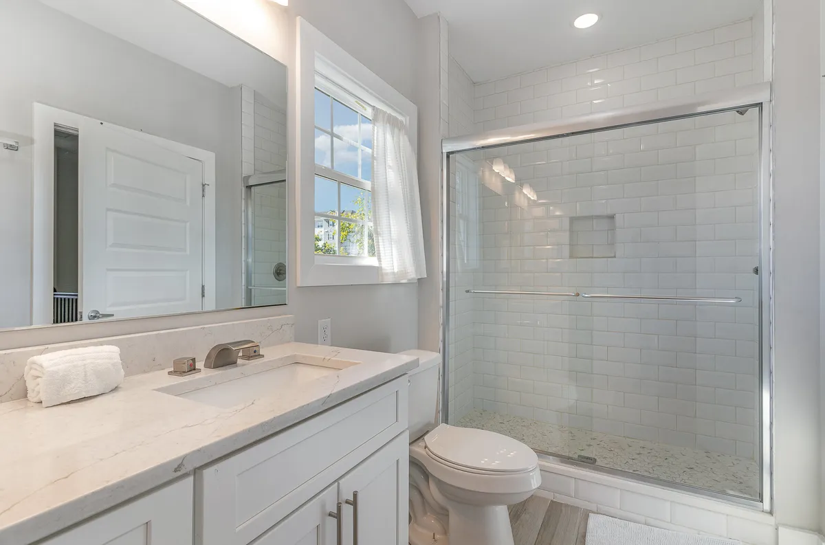 A modern bathroom featuring a sleek vanity with a sink, a shower stall, and a window letting in soft light. The fixtures are contemporary and the overall mood is tranquil and spa-like.