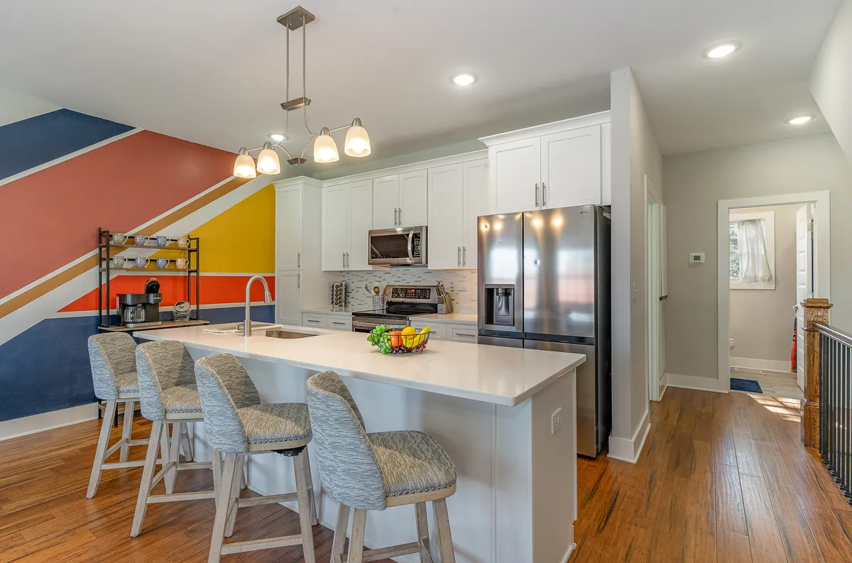 This interior image features a spacious kitchen island with a vibrant accent wall and modern appliances. The space is well-lit and designed for both cooking and socializing, representing a central gathering spot for guests. The setup hints at curated kitchen essentials and a welcoming atmosphere for entertaining.