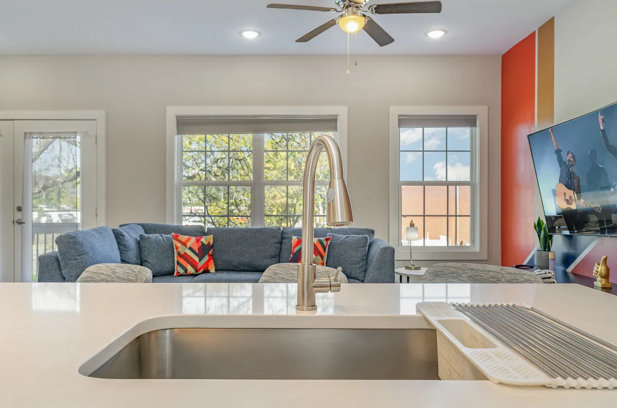 A cozy living area with a blue sofa, colorful cushions, a television, and a glimpse of the kitchen sink. The inviting atmosphere suggests a versatile space for relaxing, entertaining, and spending time with family or pets.
